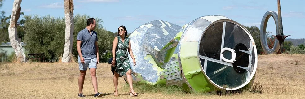 A couple walks past a large sculpture of an crushed aluminum can 