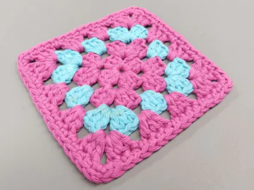 A pink and blue granny square on a grey background.