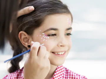 A little girl having some pink and white flowers painted on her face.