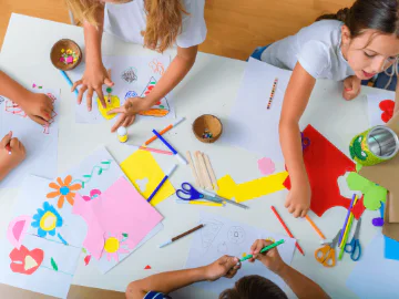Children painting, drawing and cutting paper at a table 