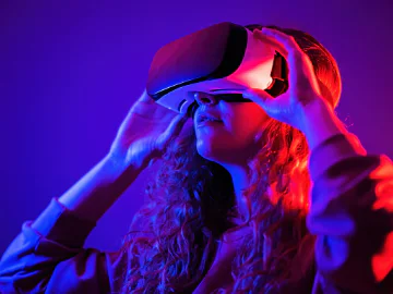 A teenage girl holding a VR headset to her eyes 