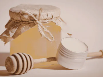A jar of honey, a honey dripper and an open jar of balm
