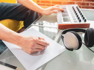 A person playing with a piano keyboard while writing something down on a piece of paper.