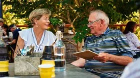 An elder man with a woman looking at a a menu at an outdoor cafe
