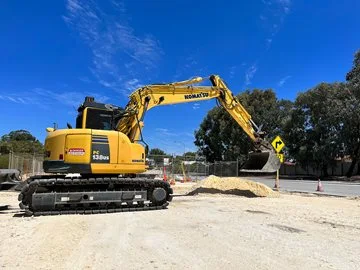 A large yellow excavator sits on crushed limestone. It is scooping up sand.