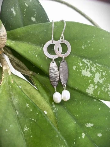 handcrafted silver earrings on a vibrant plant leaf 