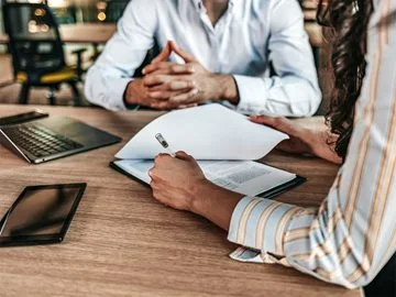 Two people looking at papers and a laptop in a business setting.