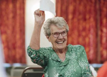 An elderly woman smiling as she holds up a winning bingo card