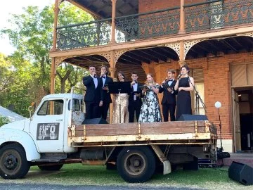 A photo of artists singing while standing on the back of an old  track