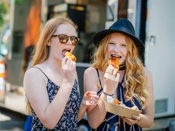 Two women eat pastries bought from a food truck