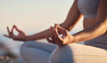 A cropped image of a person meditating with crossed legs and their hands out on their knees
