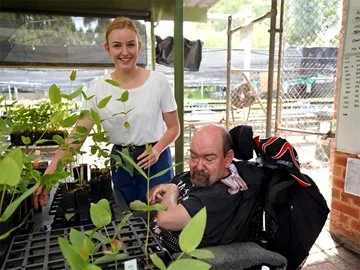 A volunteer carer helps a man with disabilities pot seedlings.
