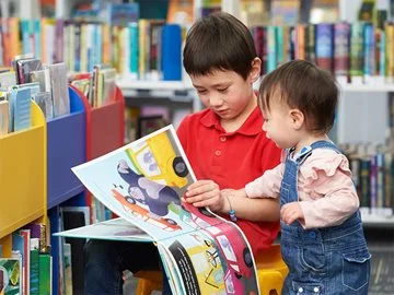 Two children read a book together in a library