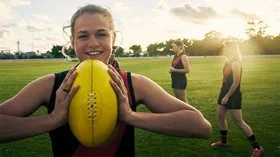 A female AFL player holding a footy