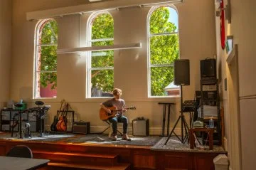 man playing acoustic guitar on a stage surrounded by various musical equipment