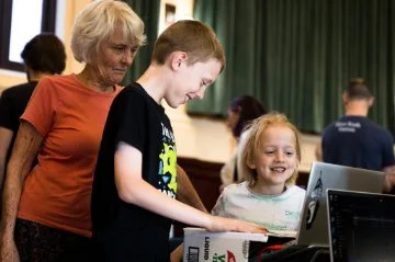Some children and an older woman interacting with some tech tools