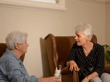 Two senior aged women sitting in armchairs talking. 