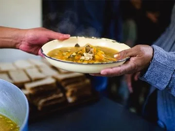 A bowl of soup is handed from one person to another