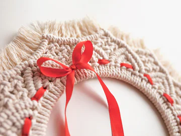 A close up of a macrame Christmas wreath with a red ribbon