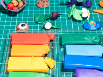 Rainbow clay and clay creations on a green craft board. 