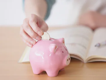 Close up off hand putting coin in a piggy bank. 