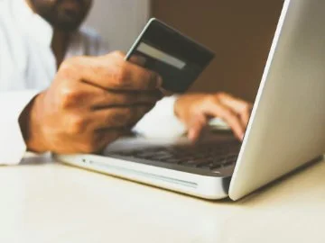 Man holding and reading a credit card as he types on his laptop