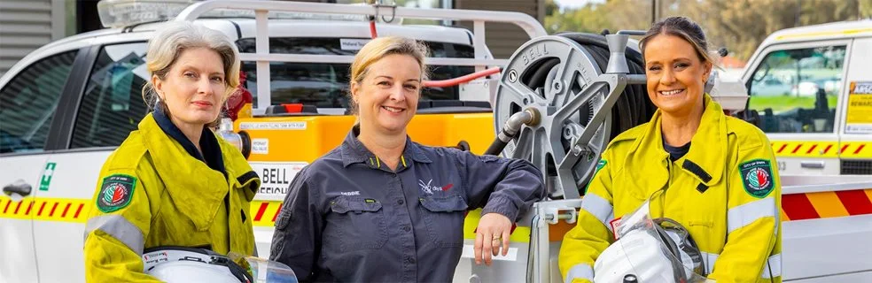 Three female firefighters standing in front of a vehicle